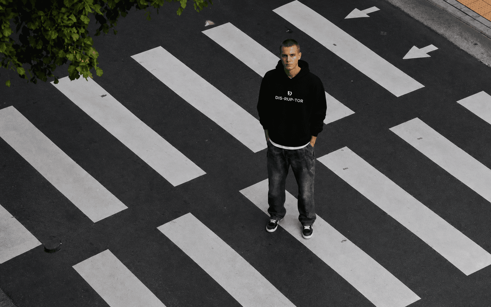 Model wearing a black Disruptor hoodie on a city crossing