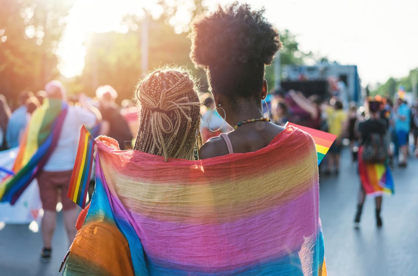 Two people wrapped in a Pride flag at a march